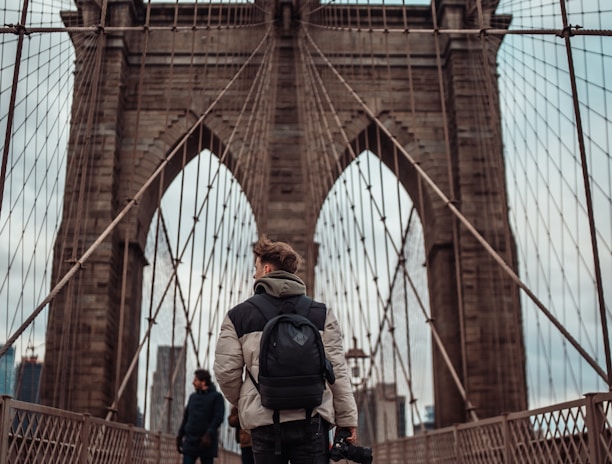 man in black jacket and black pants standing on brown bridge