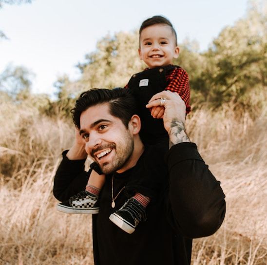 man in black jacket carrying baby in red and white checkered shirt during daytime